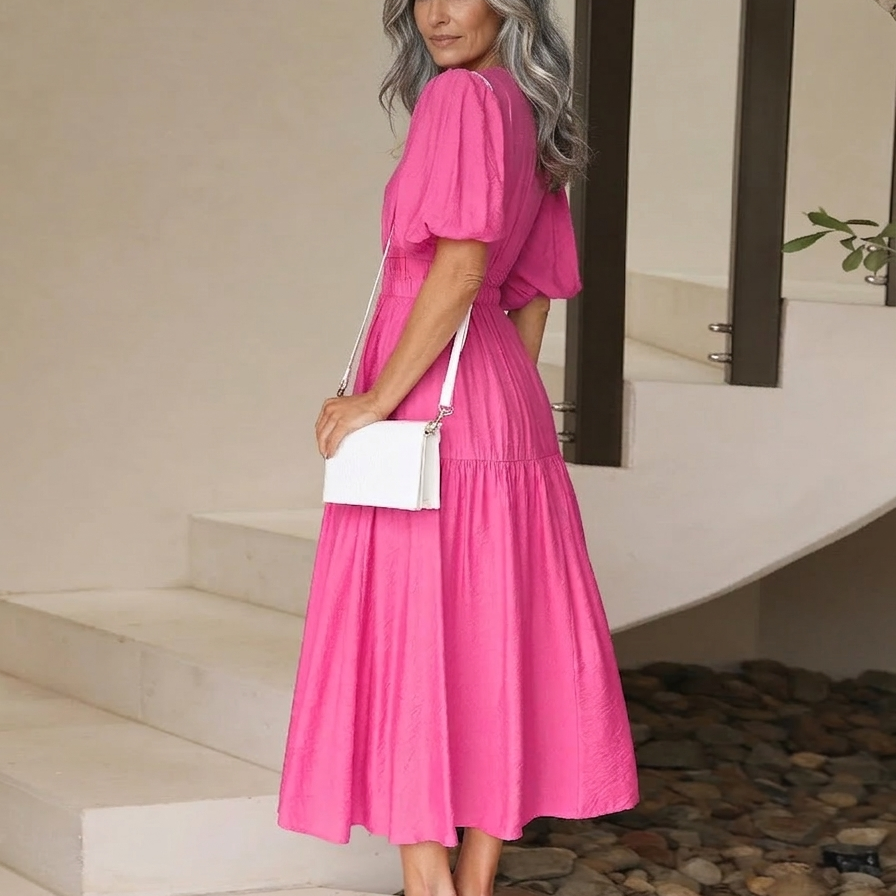 Woman in a pink dress holding a white handbag on a staircase.